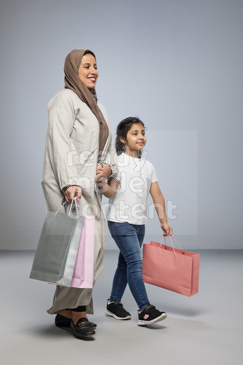 Mom and daughter holding shopping bags on gray background