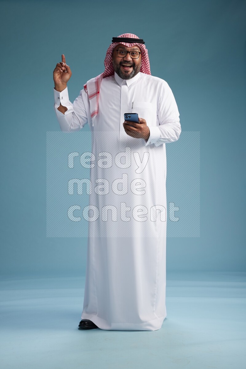 Saudi Man with shimag Standing texting on phone on blue background