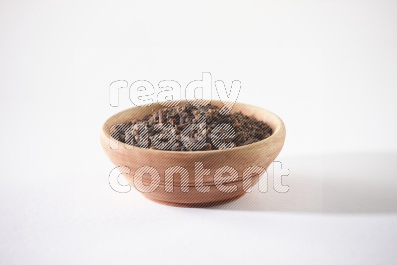 A wooden bowl full of cloves on a white flooring