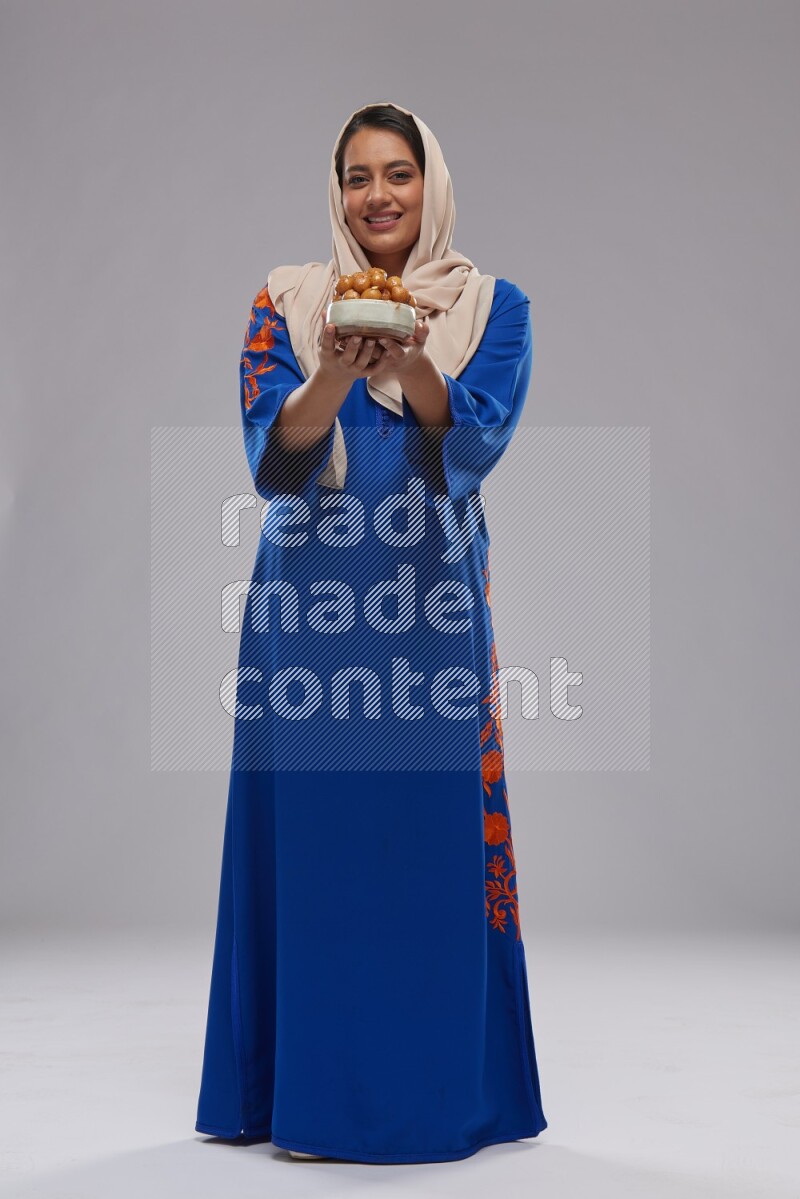 A Saudi woman standing wearing Jalabeya holding a plate of luqaimat