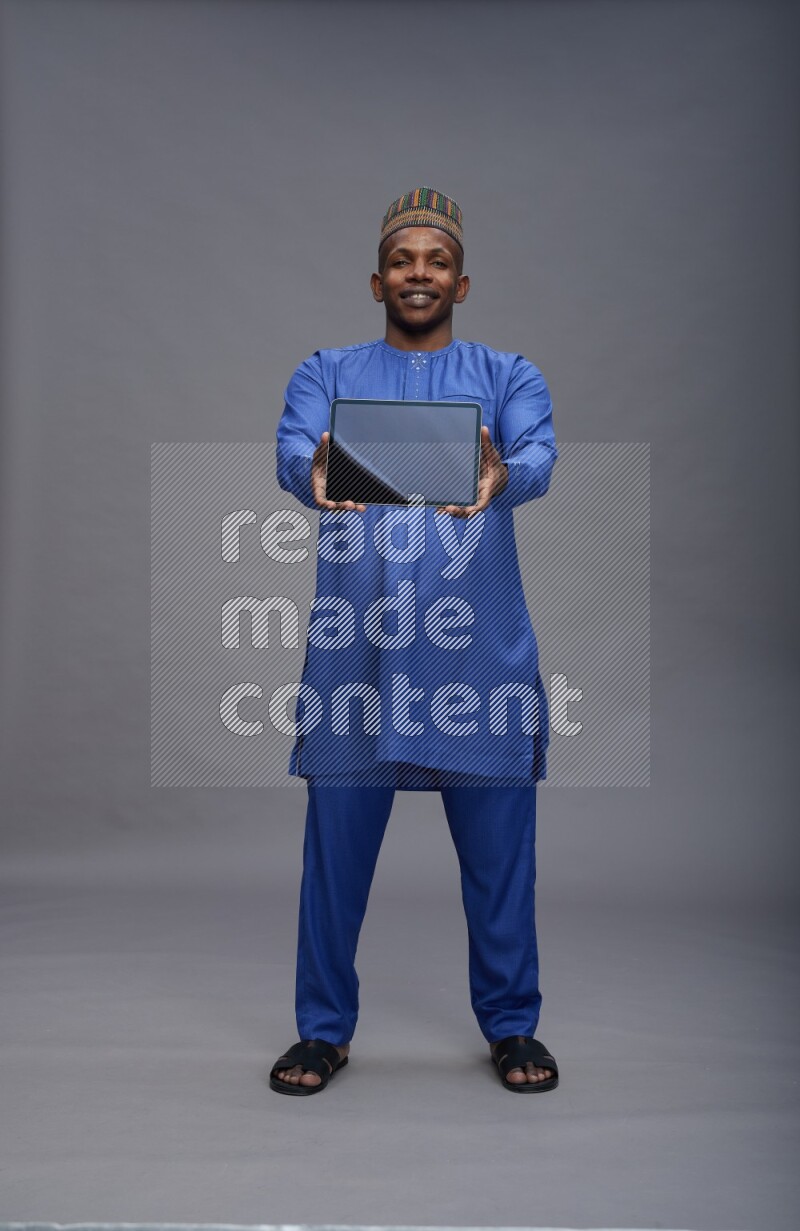 Man wearing Nigerian outfit standing showing tablet to camera on gray background