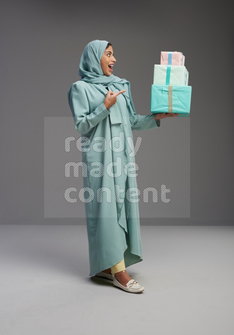 Saudi Woman wearing Abaya standing holding gift box on Gray background