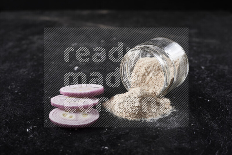 A glass jar full of onion powder flipped with some spilling powder on black background