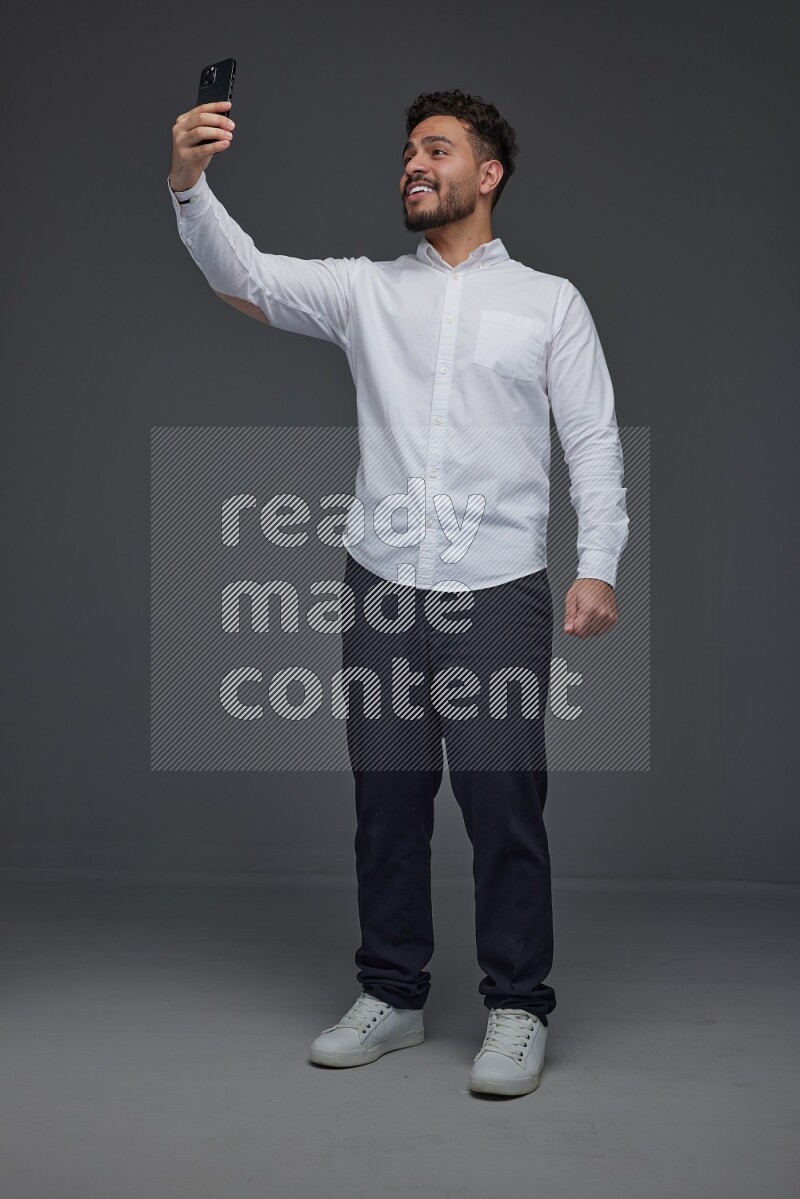 A man wearing smart casual and taking selfie with his phone eye level on a gray background