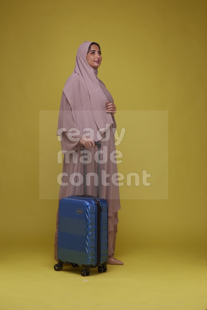 A woman With suit Case on a Yellow Background wearing Brown Abaya with Hijab