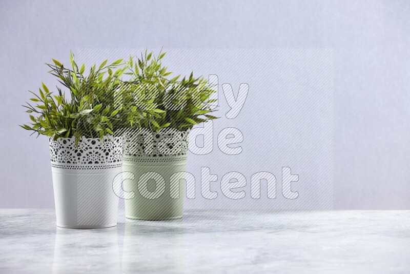 Two different artificial plants in white and green decorative pots on grey marble background