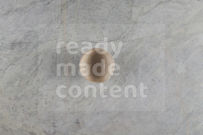 A small beige pottery bowl on grey marble background