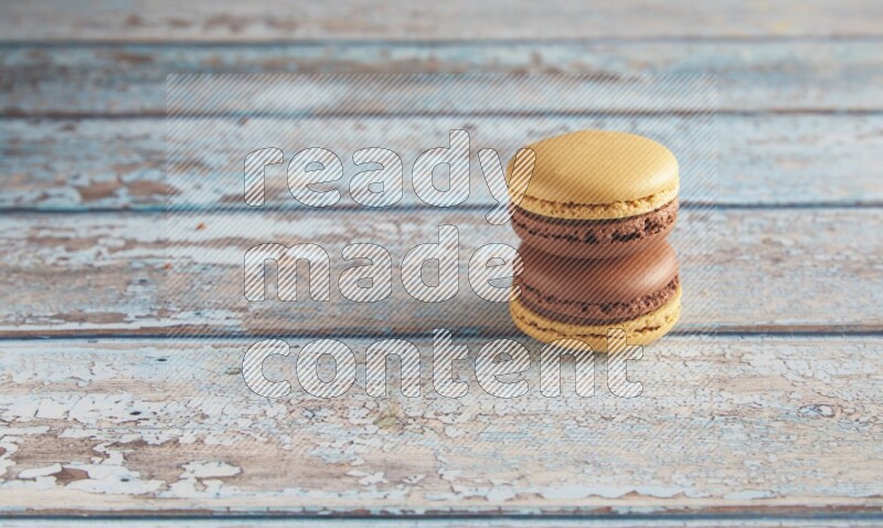 45º Shot of two Yellow and Brown Chai Latte macarons on light blue wooden background