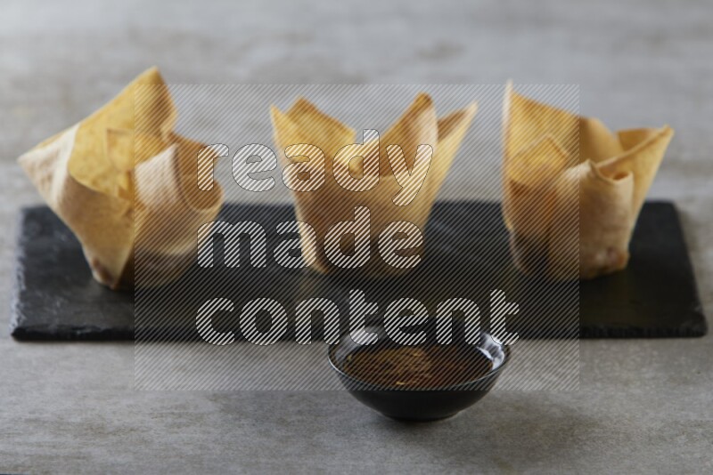 wonton cups with soy sauce ramkin on rectangle slate on grey textured counter top