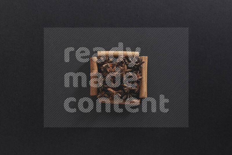 A single square of cinnamon sticks full of star anise on black flooring