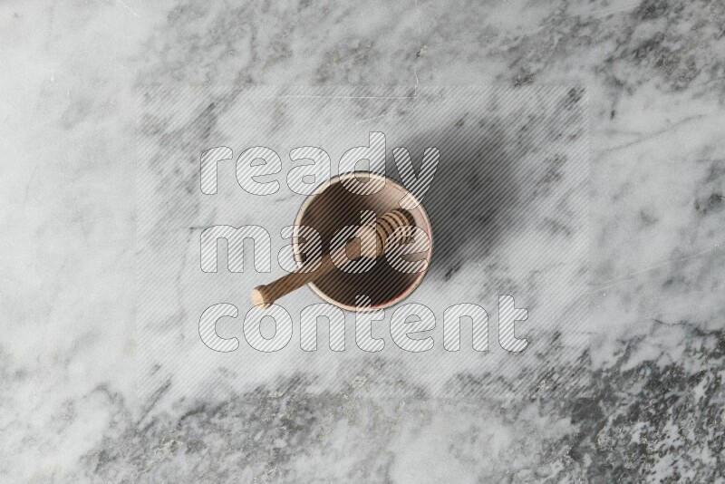 Beige pottery bowl with wooden honey dipper in it on grey marble background