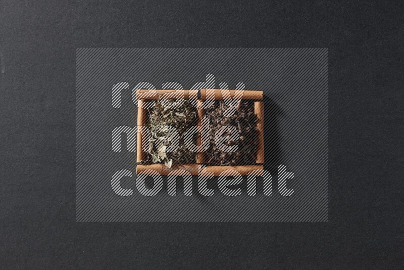 مربعان من أعواد القرفة ممتلئان بالقرنفل والريحان المجفف علي خلفية سوداء