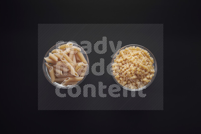 Different pasta types in glass bowls on black background
