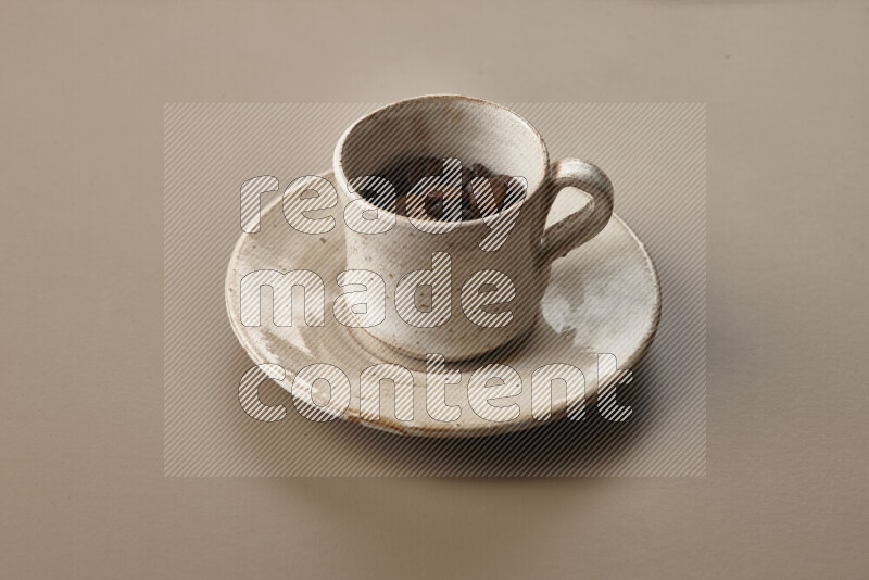 A beige pottery cup full of roasted coffee beans on beige background