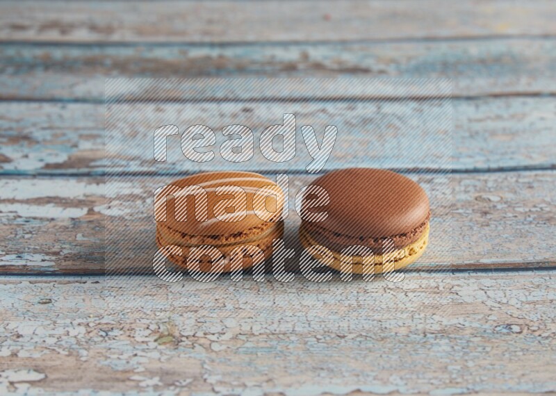 45º Shot of of two assorted Brown Irish Cream, and Yellow, and Brown Chai Latte macarons  on light blue background