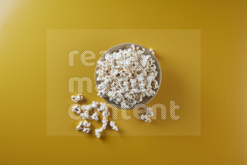 A multicolored ceramic plate full of popcorn with popcorn beside it on a yellow background in different angles