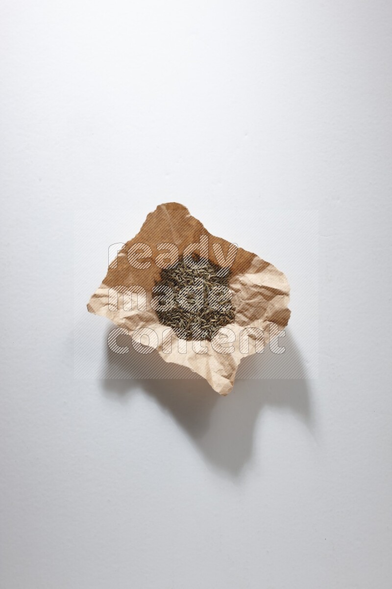 Cumin seeds in a crumpled piece of paper on white flooring