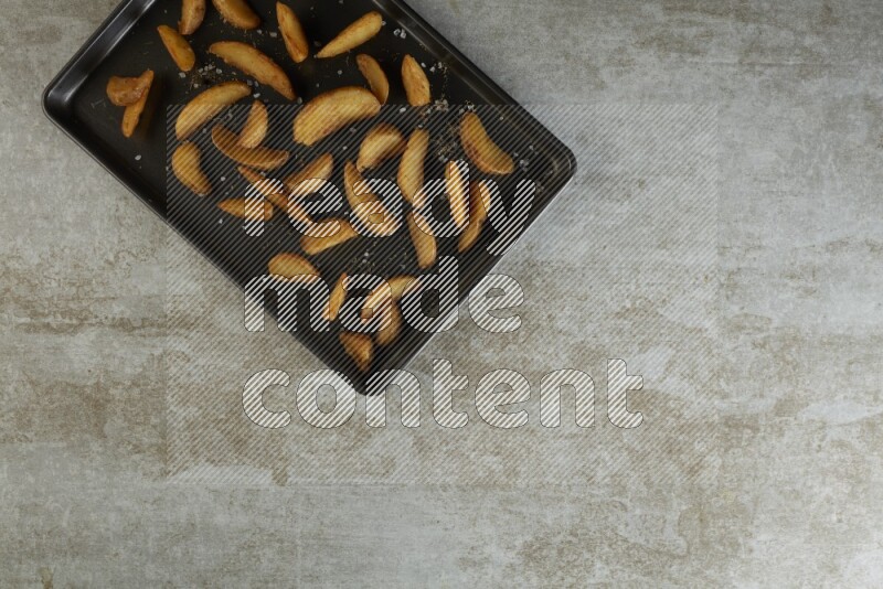 wedges potato in a black stainless steel rectangle tray on grey textured counter top