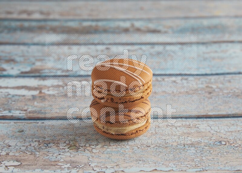 45º Shot of of two assorted Brown Irish Cream, and light brown Almond Cream macarons next to each other on light blue background