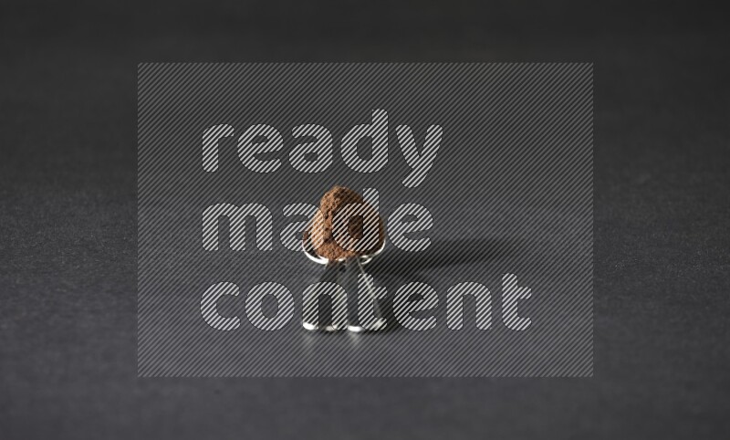 2 metal spoons on top of each other full of cloves powder on a black flooring