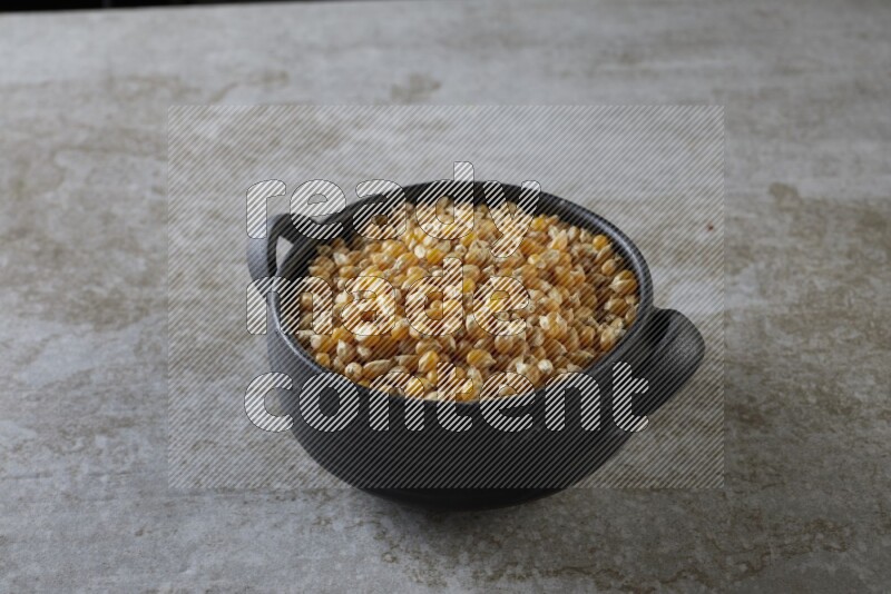 corn kernel in a black handheld ceramic bowl on a grey textured countertop