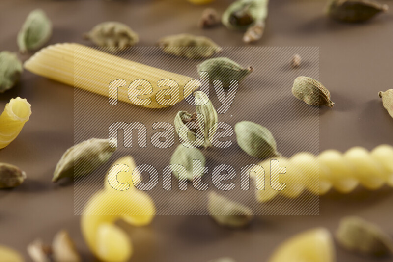 Raw pasta with different ingredients such as cherry tomatoes, garlic, onions, red chilis, black pepper, white pepper, bay laurel leaves, rosemary and cardamom on beige background