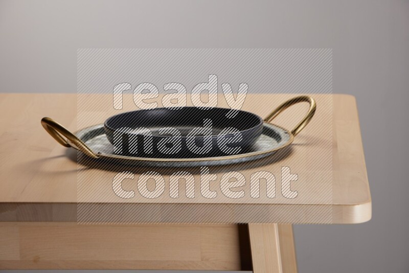 black plate placed on a rounded stainless steel metal tray with golden handels on the edge of wooden table