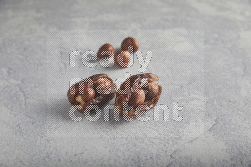 Two hazulnut stuffed dates with unroasted hazelnuts on light grey background