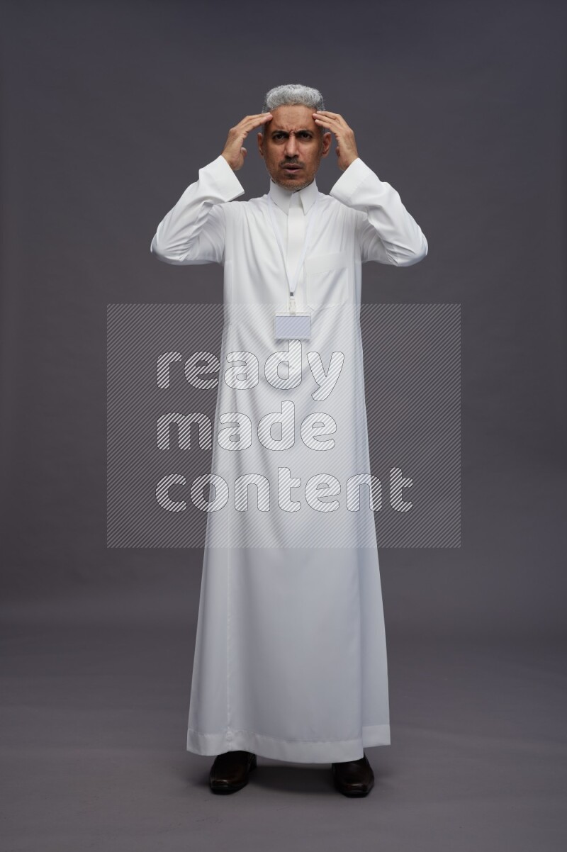 Saudi man wearing thob with neck strap employee badge standing hands on head on gray background
