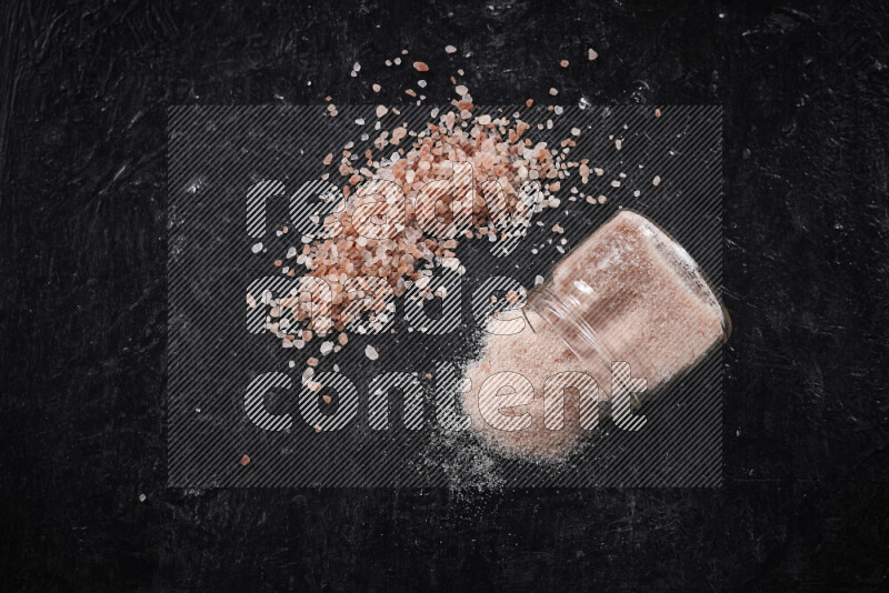 A glass jar full of fine himalayan salt with some himalayan crystals beside it on a black background