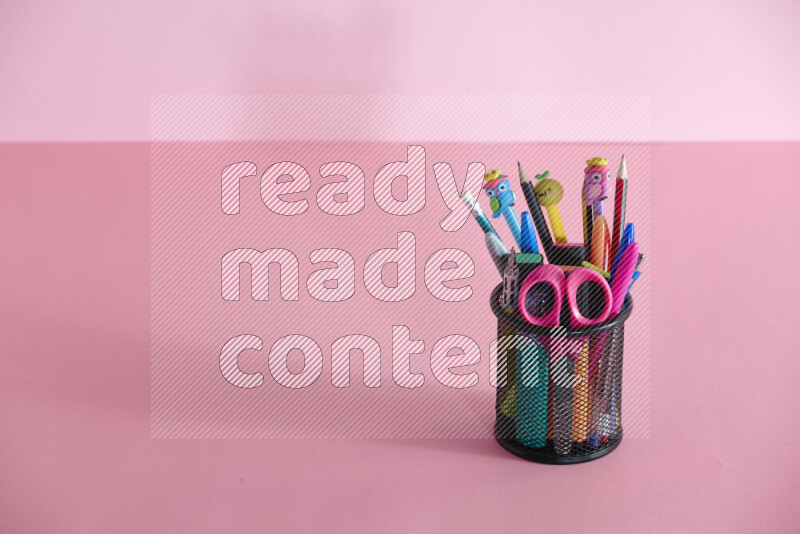 Pens, pencils and other different school supplies in a metal pen holder on rose background