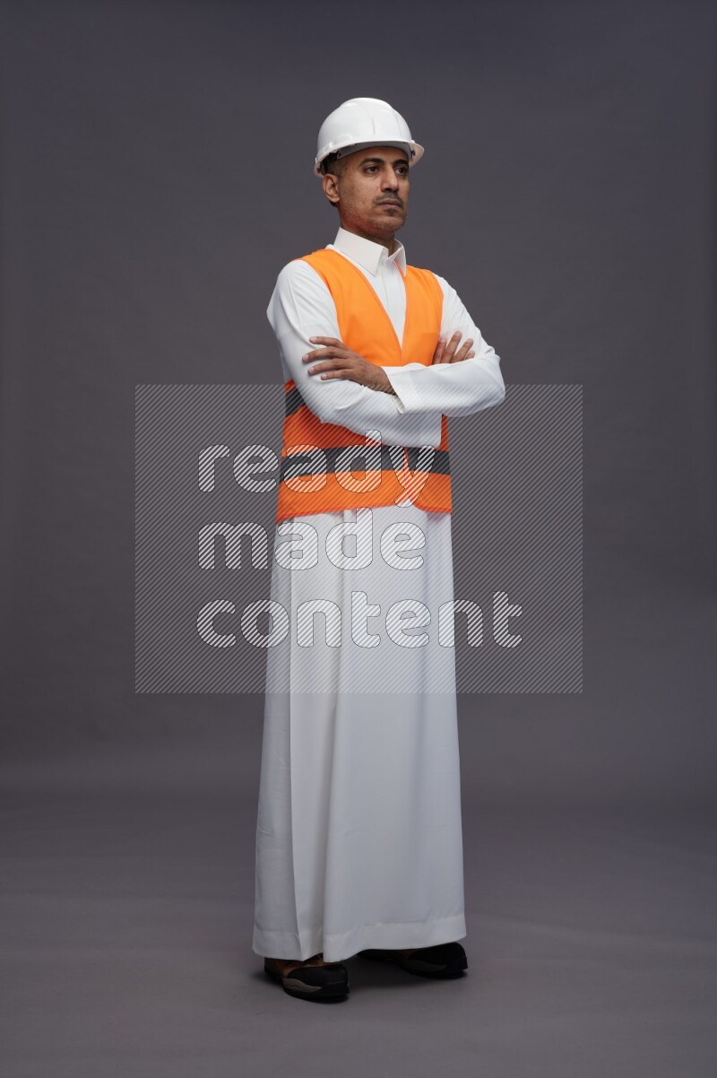 Saudi man wearing thob with engineer vest standing with crossed arms on gray background