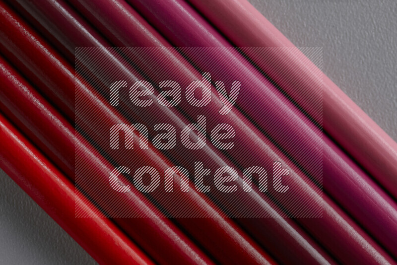 A collection of colored pencils arranged showcasing a gradient of pink and red hues on grey background