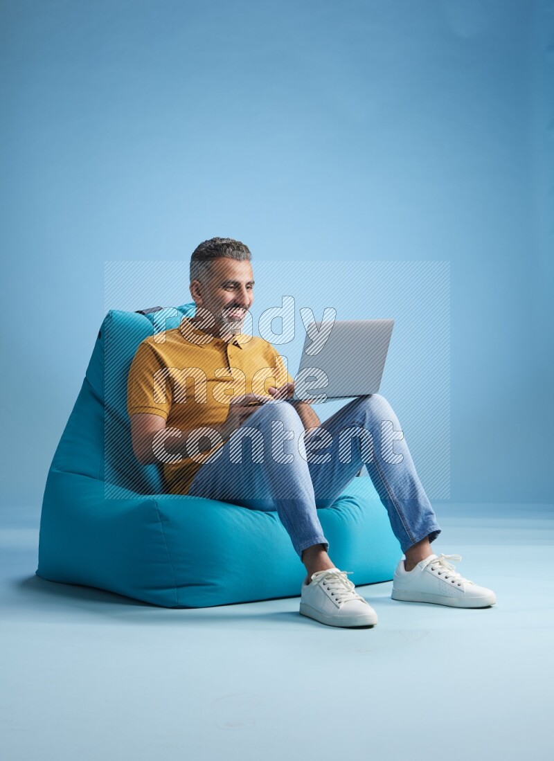A man sitting on a blue beanbag and working on laptop