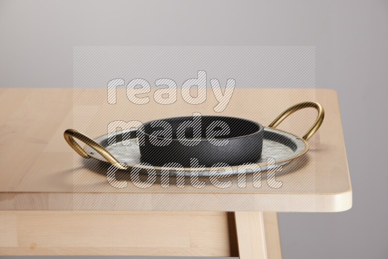 black bowl placed on a rounded stainless steel tray with golden handels on the edge of wooden table