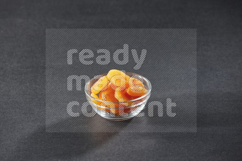 A glass bowl full of dried apricots on a black background in different angles