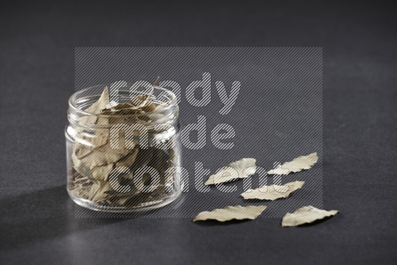 A glass jar filled with dried bay leaves on black flooring