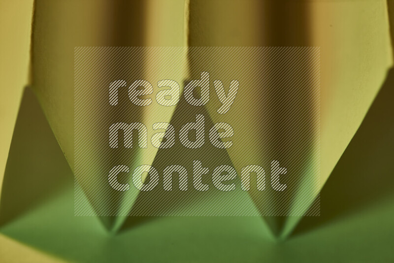 A close-up abstract image showing sharp geometric paper folds in green gradients and warm tones