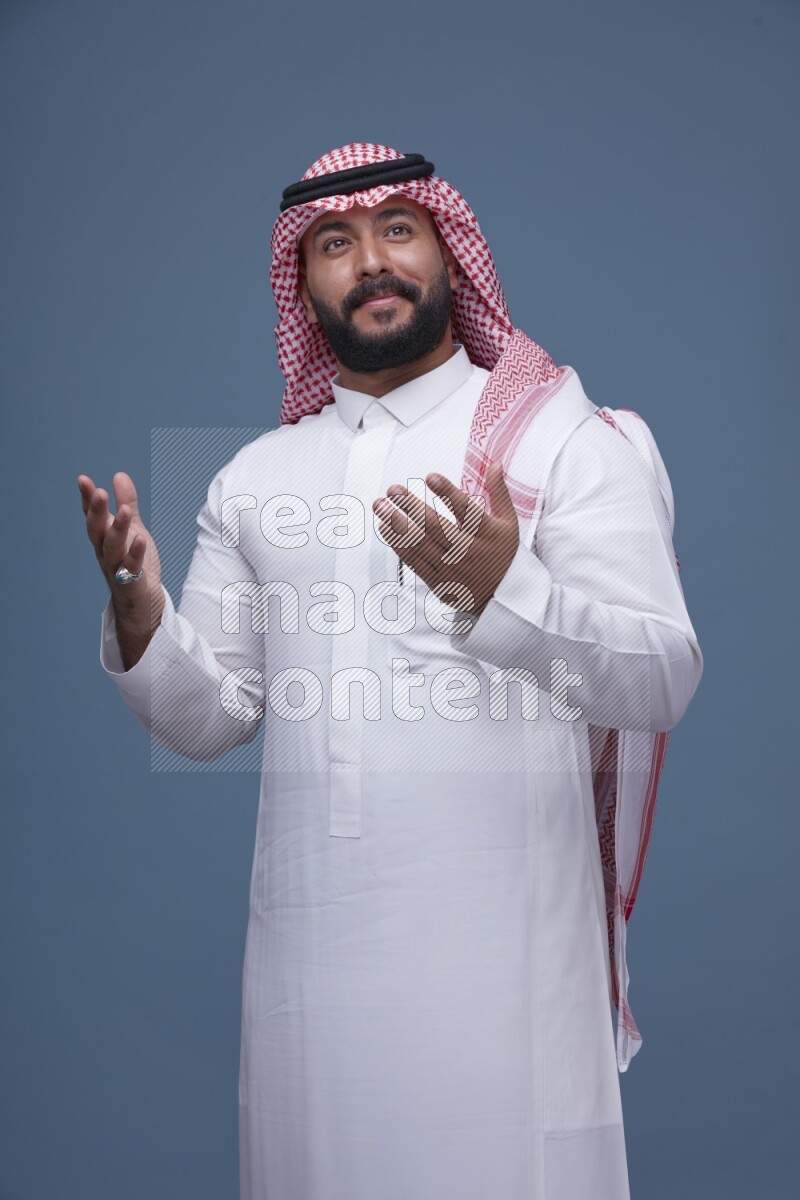 A Saudi man posing on blue background wearing Thob and Shomag