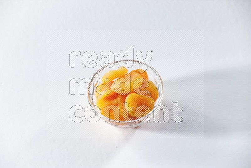 A glass bowl full of dried apricots on a white background in different angles