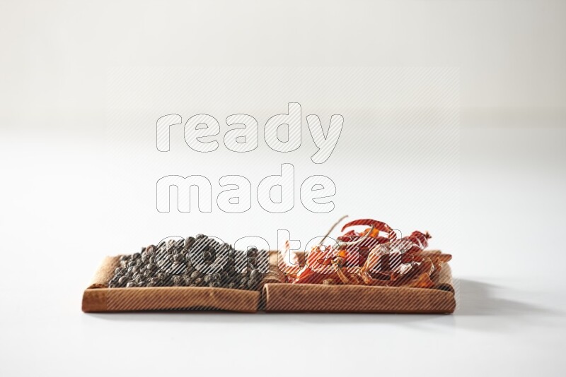 مربعان من أعواد القرفة ممتلئان بالفلفل الحار المجفف وحبوب الفلفل الأسود علي خلفية بيضاء