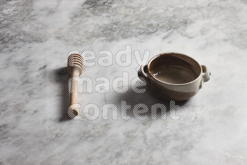 Multicolored pottery bowl with wooden honey dipper on the side on grey marble background