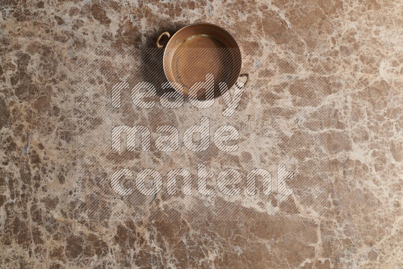 A small copper pan on beige marble background