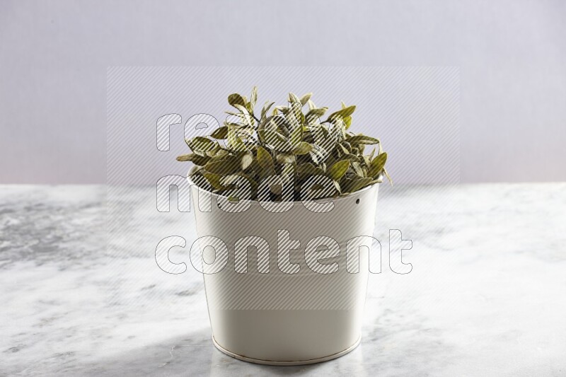 Green artificial plant in white pot on light grey marble background