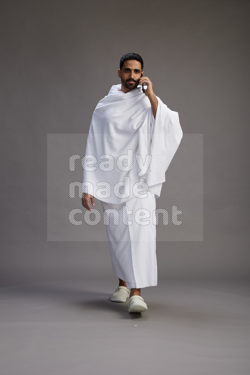 A man wearing Ehram Standing talking on phone on gray background