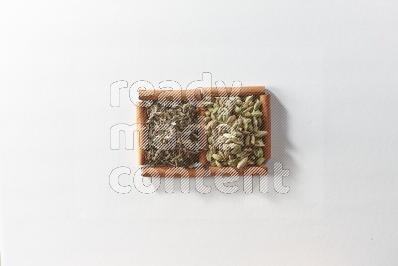 مربعان من أعواد القرفة ممتلئان بحبوب الهيل والريحان المجفف علي خلفية بيضاء