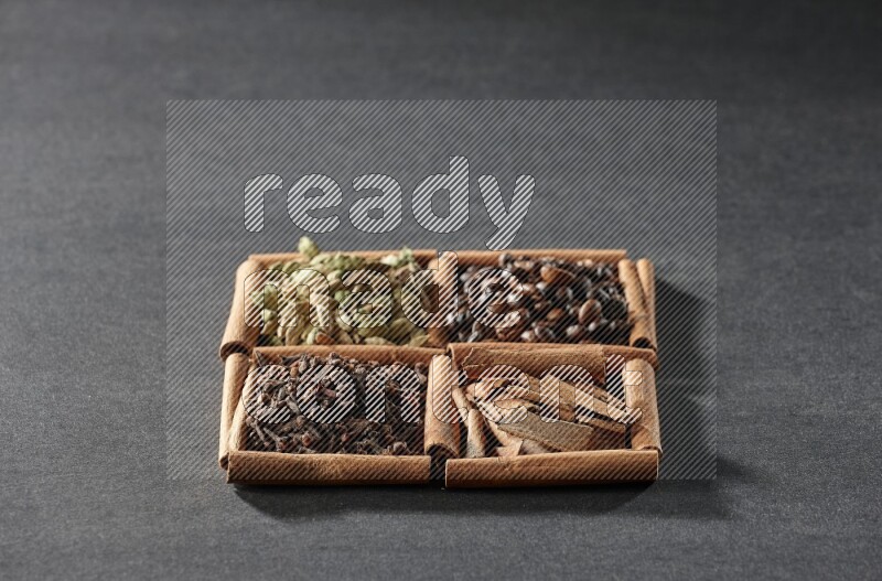 4 squares of cinnamon sticks full of coffee beans, cinnamon, cloves and cardamom on black flooring
