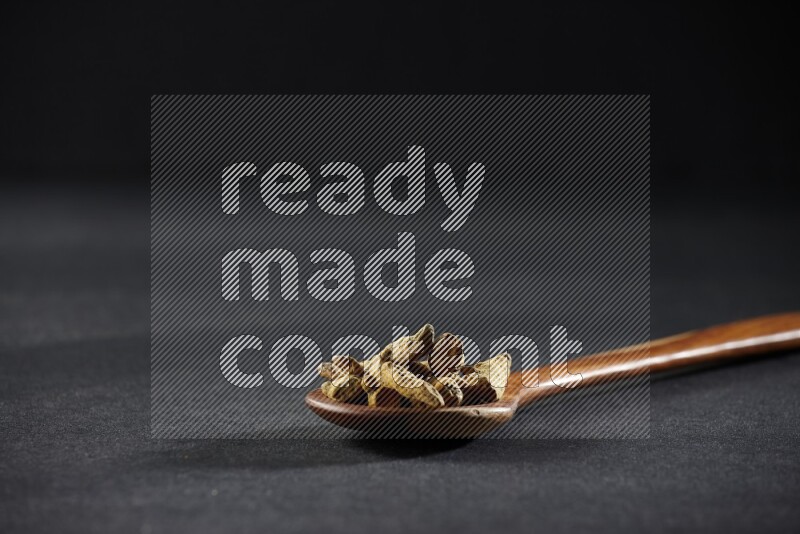 مغرفة خشبية ممتلئة بأصابع الكركم المجففة على خلفية سوداء