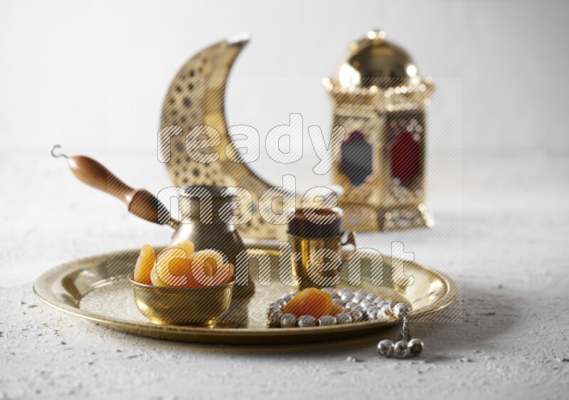 Dried apricots in a metal bowl with coffee and prayer beads on a tray beside lanterns in a light setup
