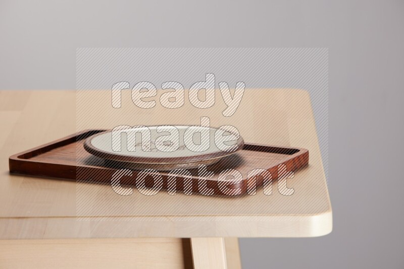 multi-colored pottery Plate placed on a rectangular wooden tray on the edge of wooden table
